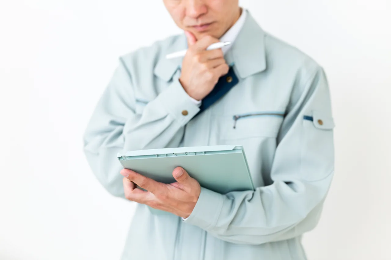 手元の資料を見ながら考える作業着の男性