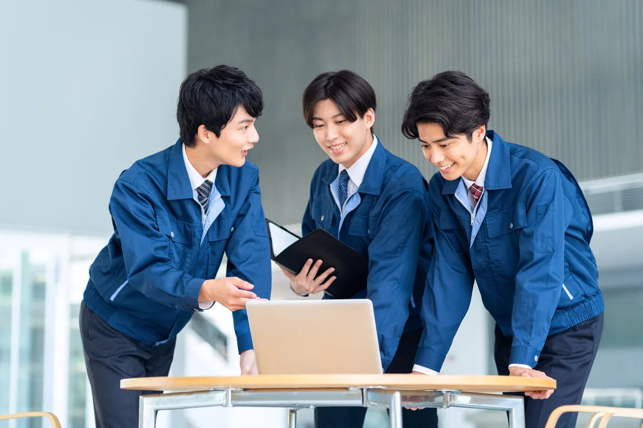作業着でパソコンを見ながら打ち合わせる社員